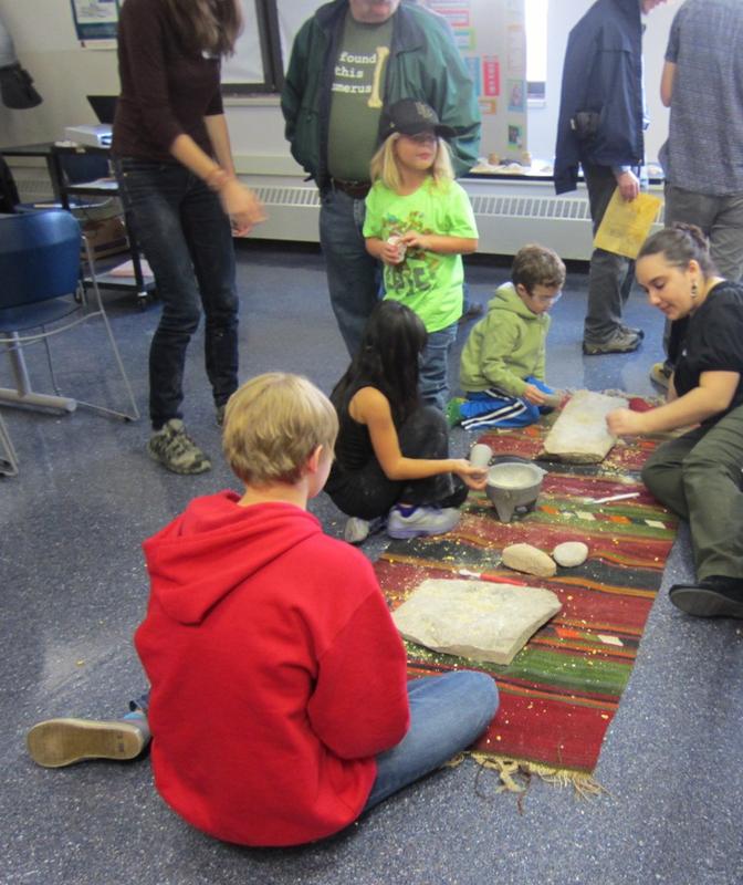 Children learn to grind grain the prehistoric way