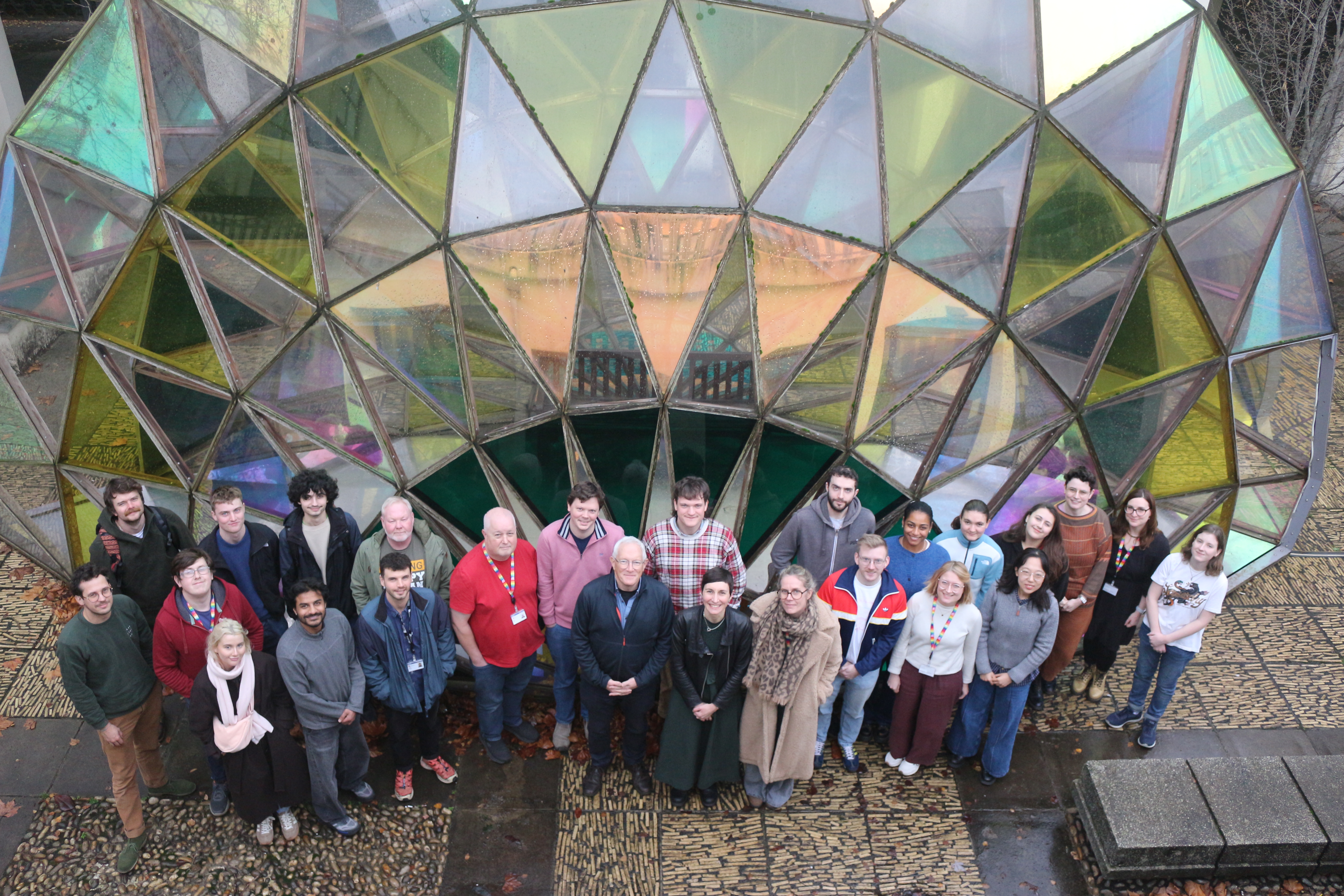 Group photo of the University of about 20 members of the Bristol Organic Chemistry Team looking up at a camera in front of a building.