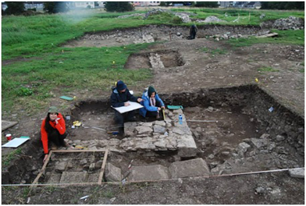 Cloister wall and buttress being documented in Cutting 5 (Cutting 4 is visible in the background). In front of the wall is a path made from the arch stones of the cloister arcade