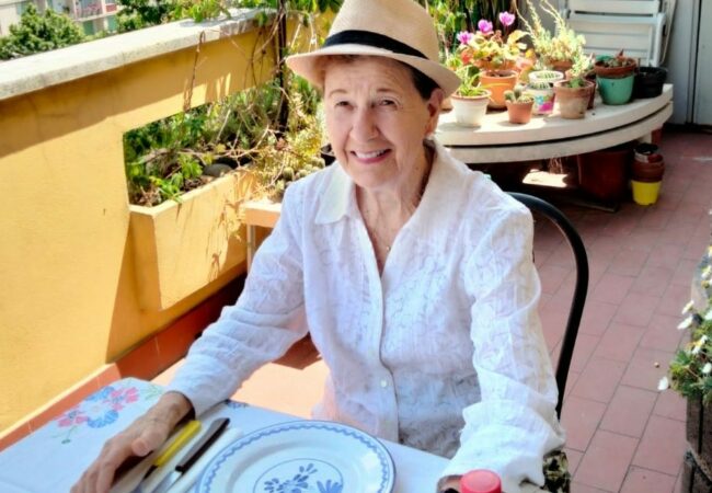 Nancy de Grummond in a hat sitting at a table.